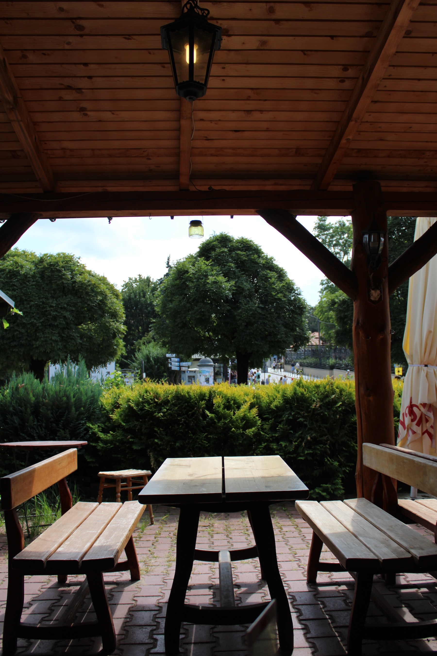 An empty outdoor seating booth at the restaurant. There's a nice lantern above, a wooden awning, and shrubbery dividing the dining area from the road.