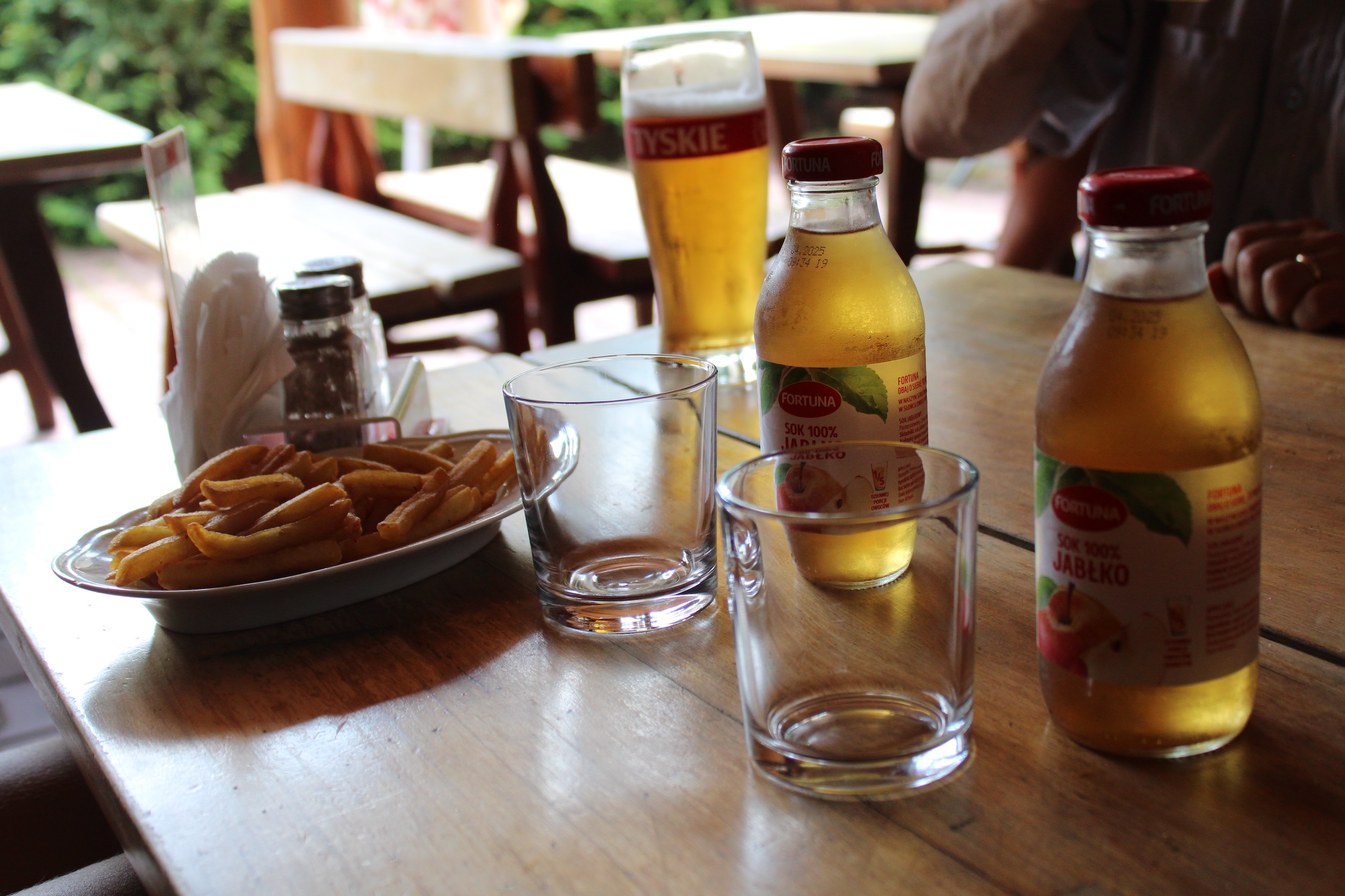 Our appetizers - fries on a oblong plate, a pint of beer, and two apple juices. The sun lights up the green color of the drinks.
