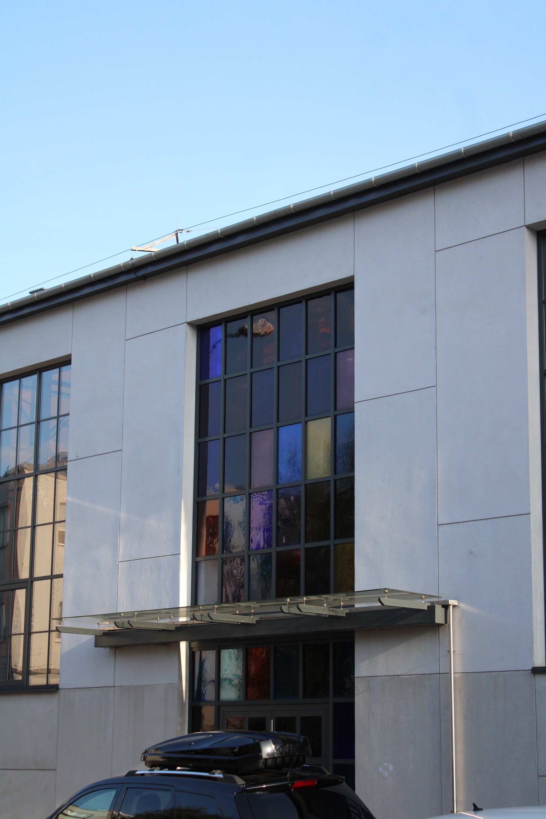 Colored stain glass windows decorate the space above a concrete building's entrance.