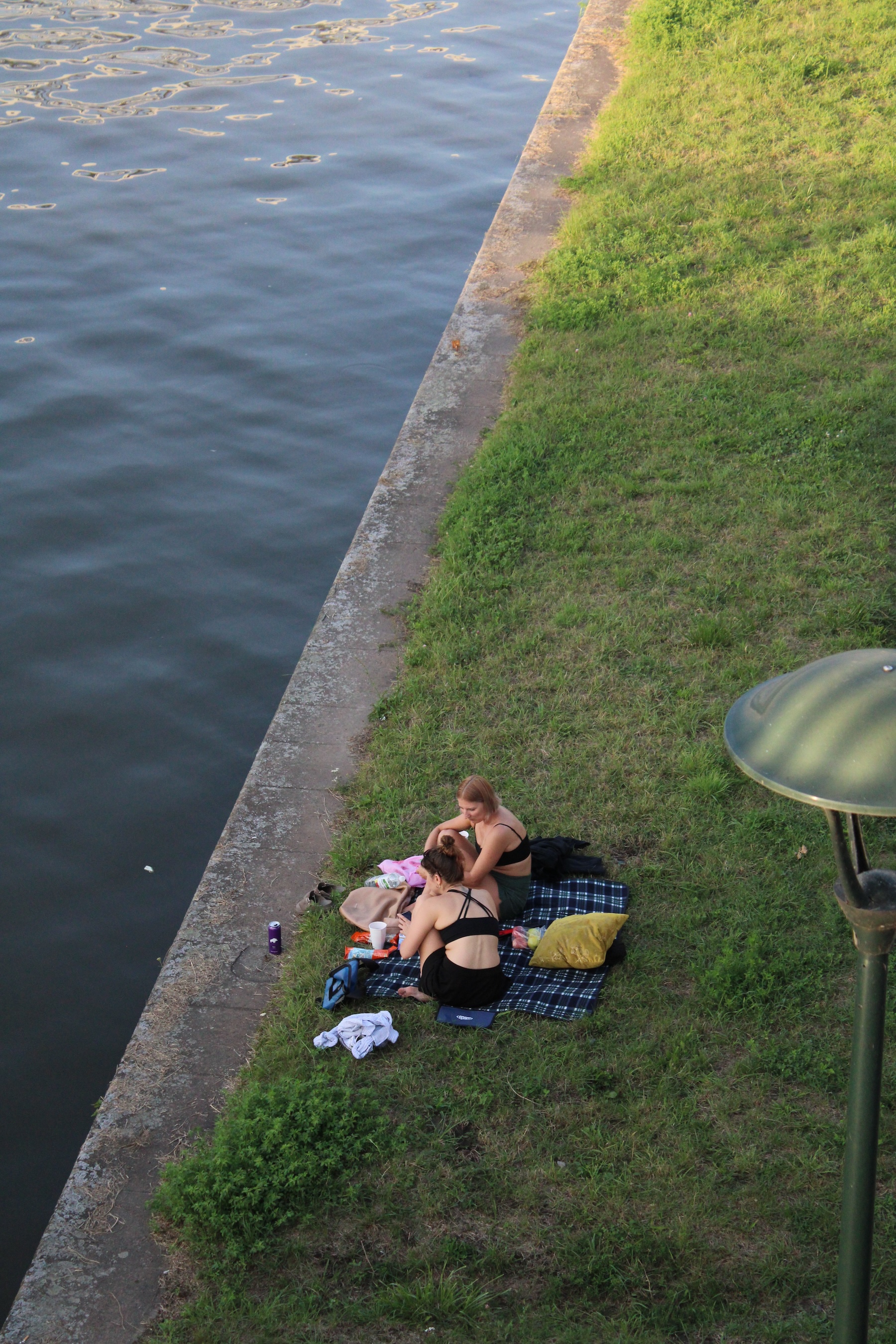 Two girls have a picnic on the side of a banked river.