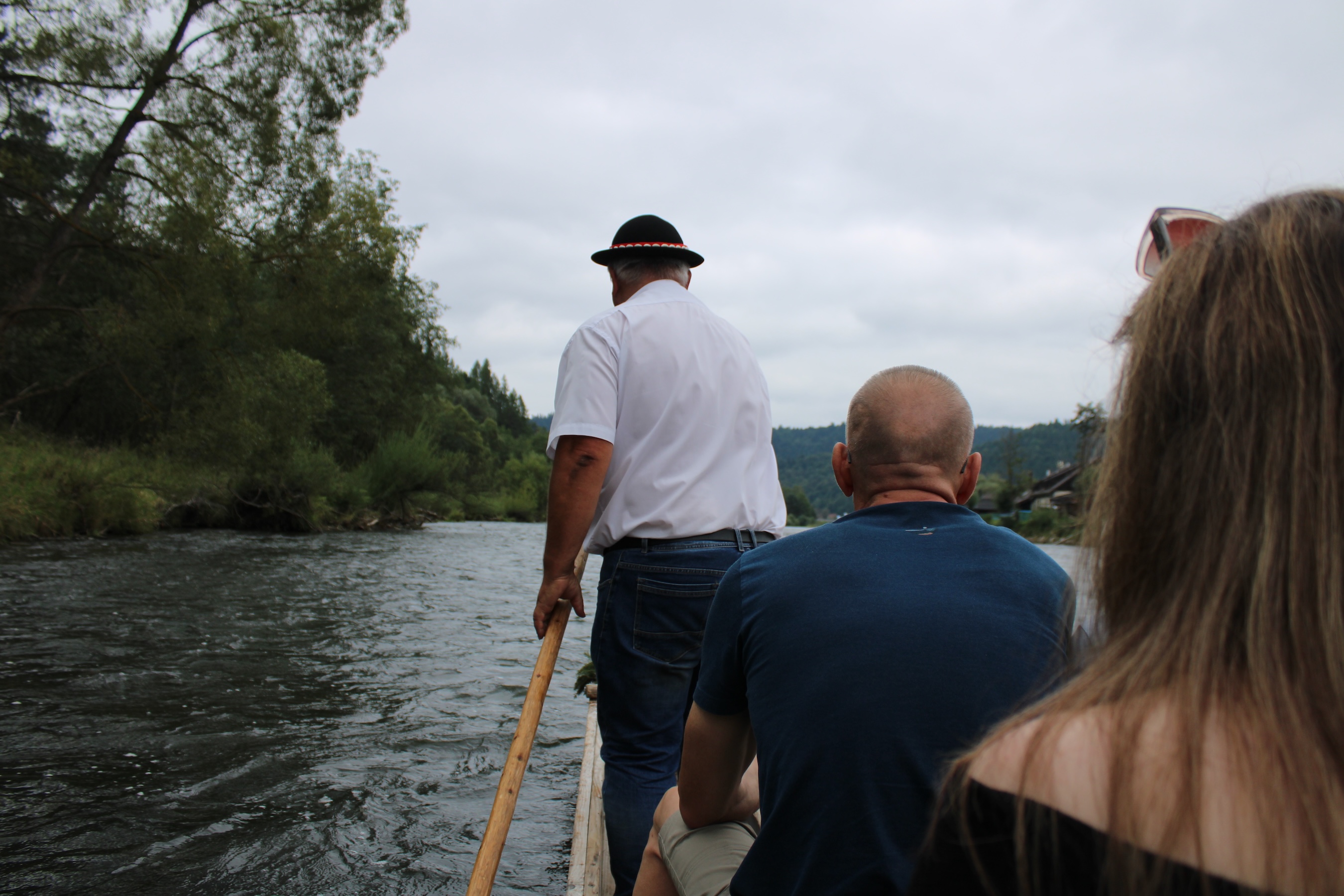 The driver at the front of a boat. He was using a wooden stick about 12 feet long to guide the boat along the shallow river.