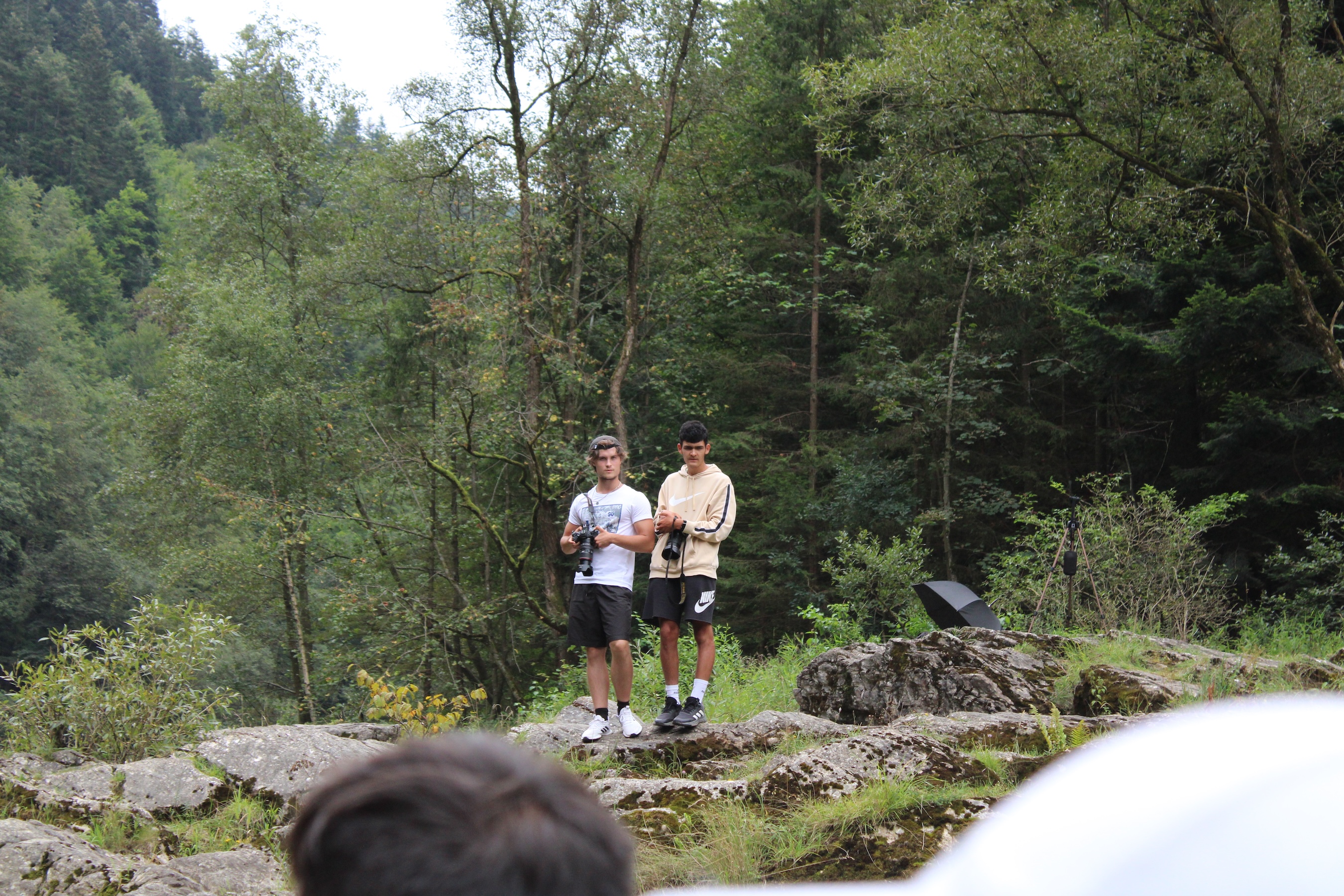 Two boys with cameras perch on top of a rocky outcropping.