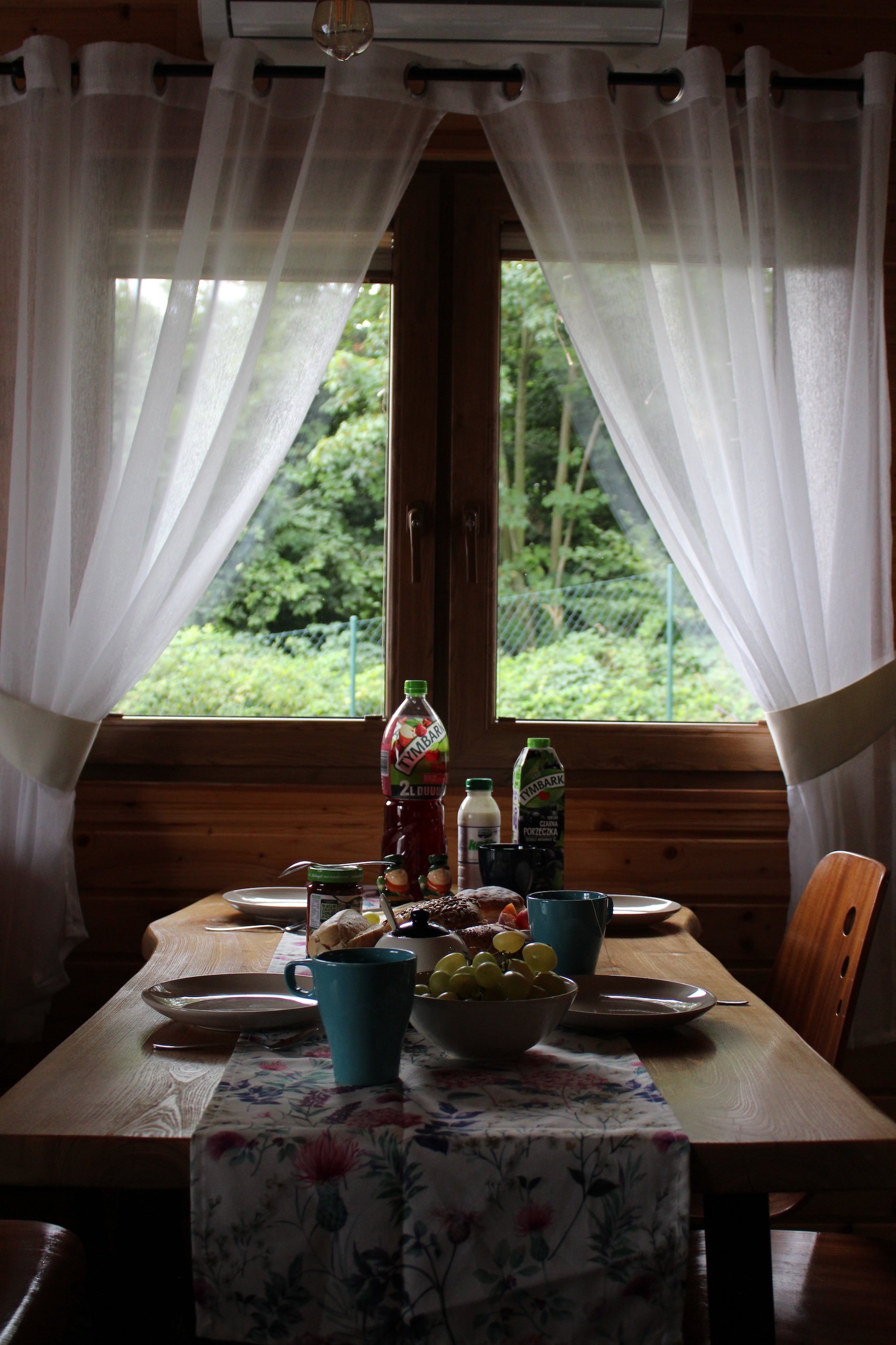 Breakfast in our accomodation. Two half-draped windows light the table with drinks and empty plates.