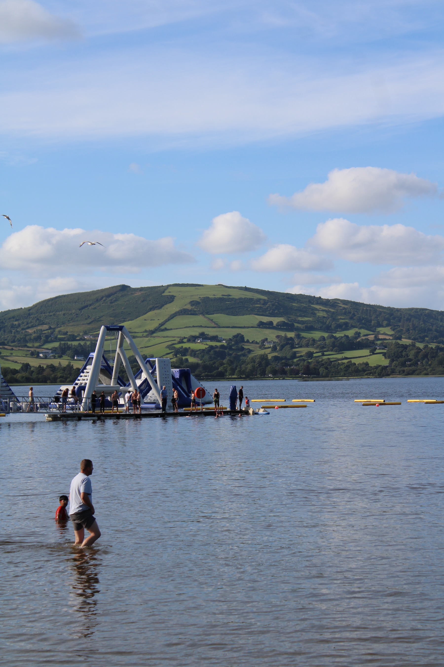 A floating waterpark on a lake with a big green hill in the background
