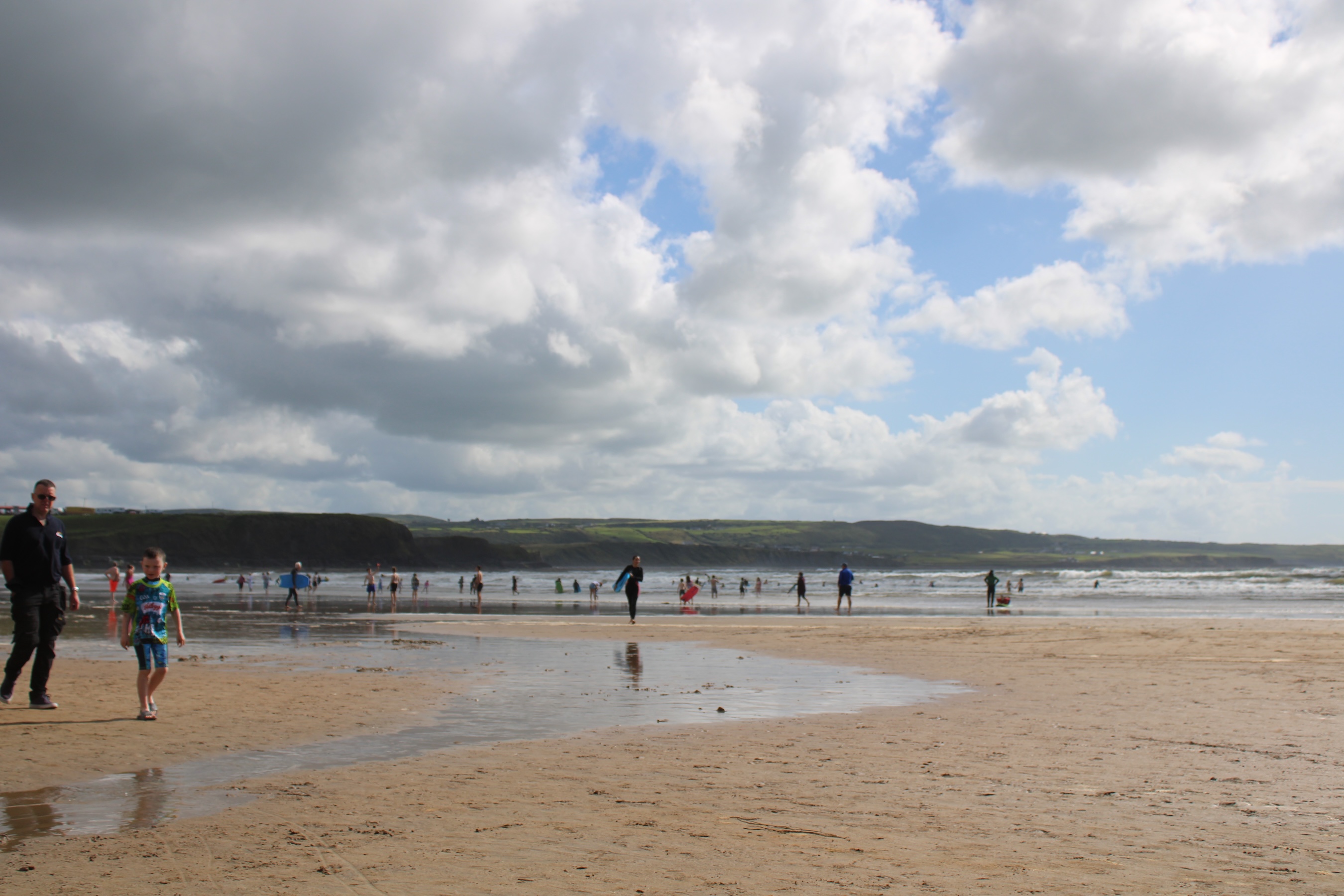 A cloudy sky is mirrored off the thin water on the beach