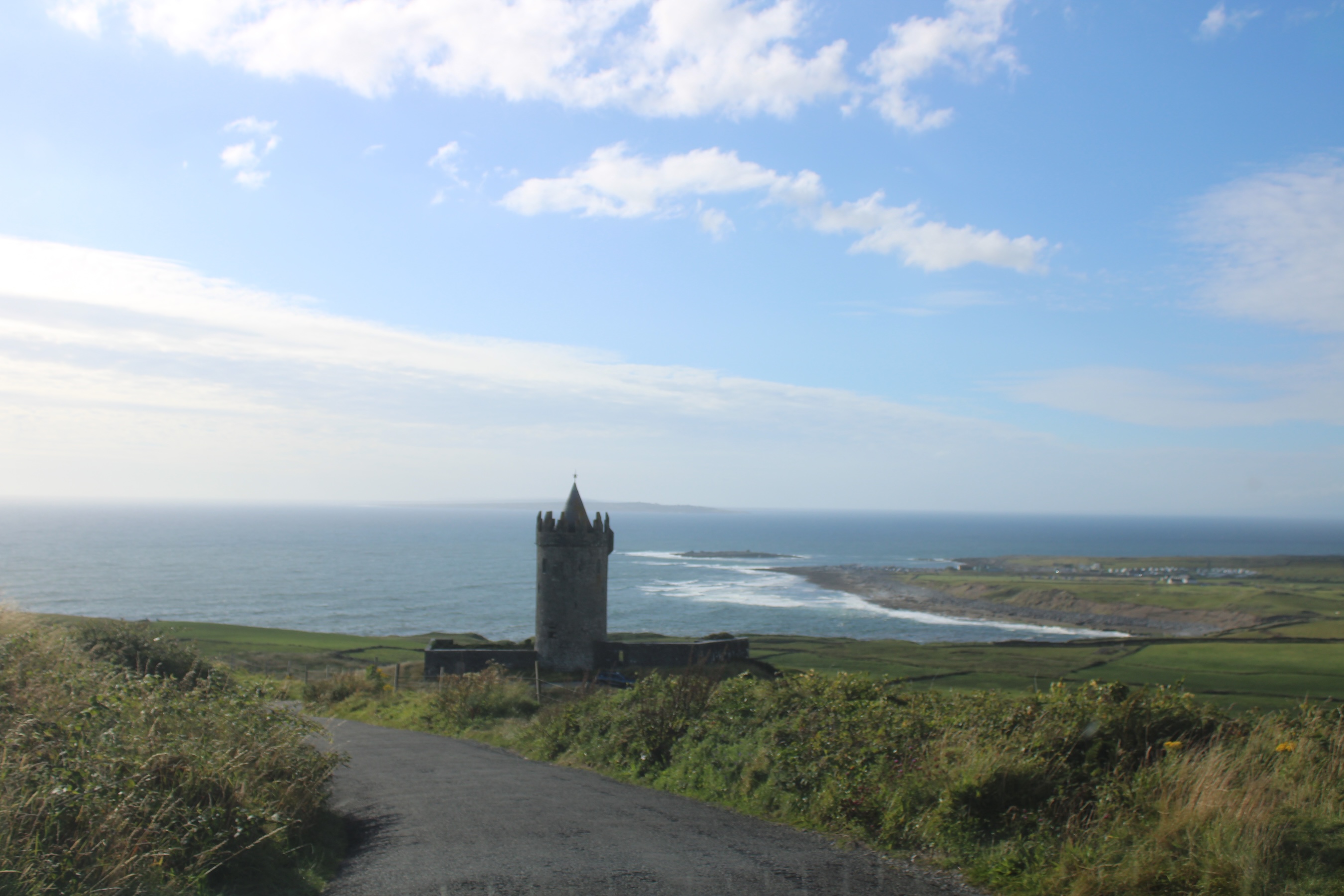 The narrow road wraps aruond a castle. The Doolin coast is visible in the back