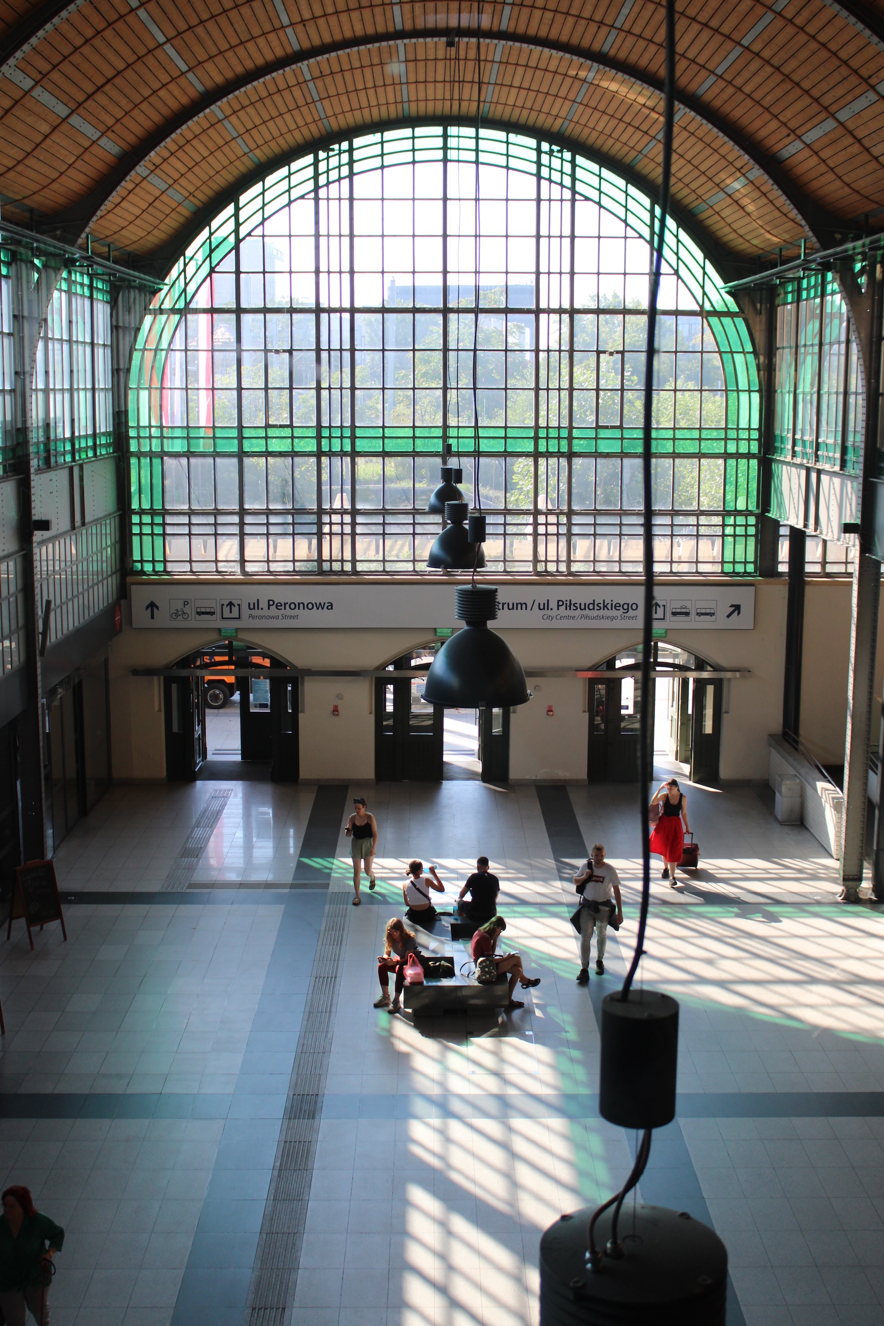One end of the train station with a giant glass wall casting light on people walking in