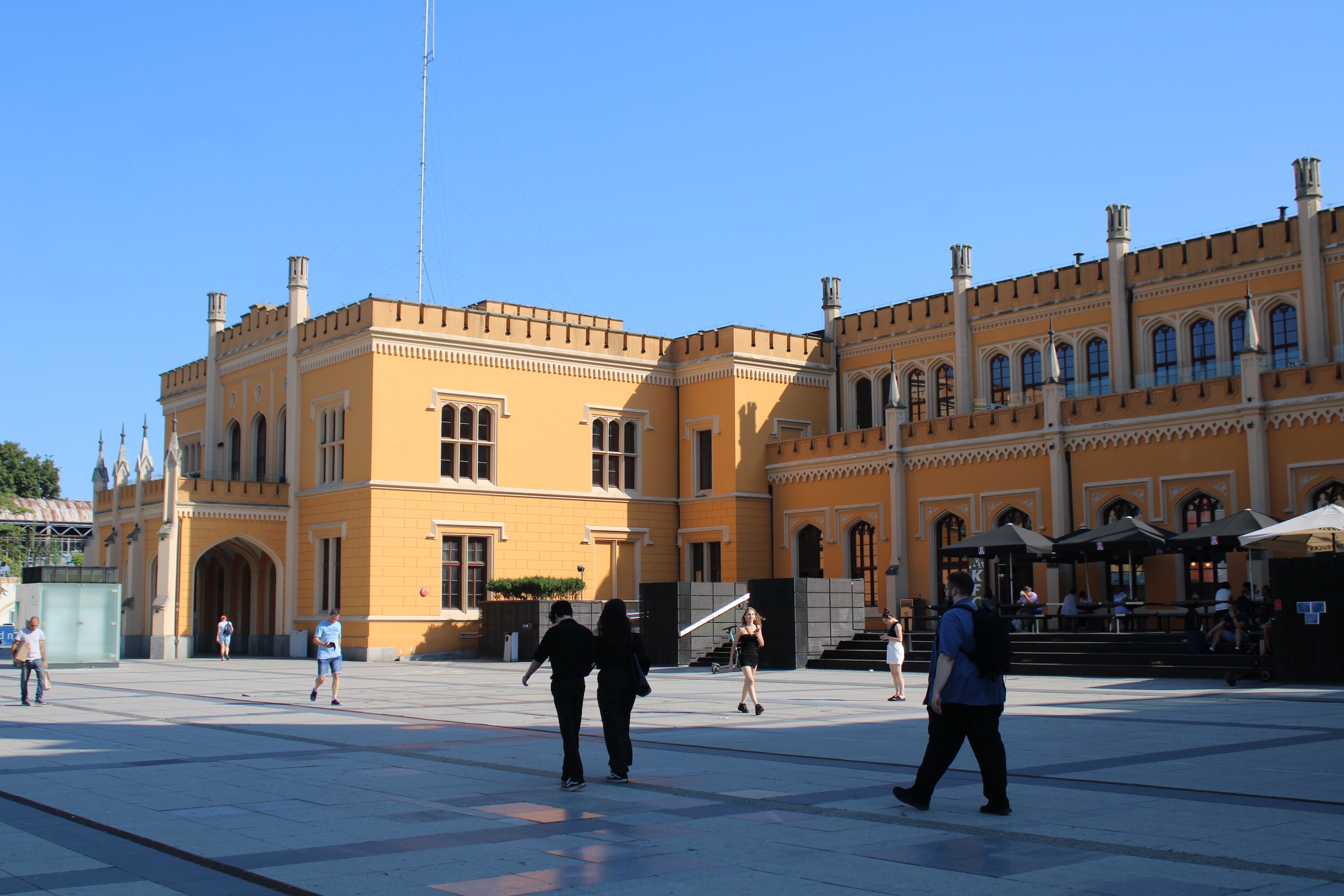The brightly-colored Wroclaw train station against a blue sky and people walking on the square