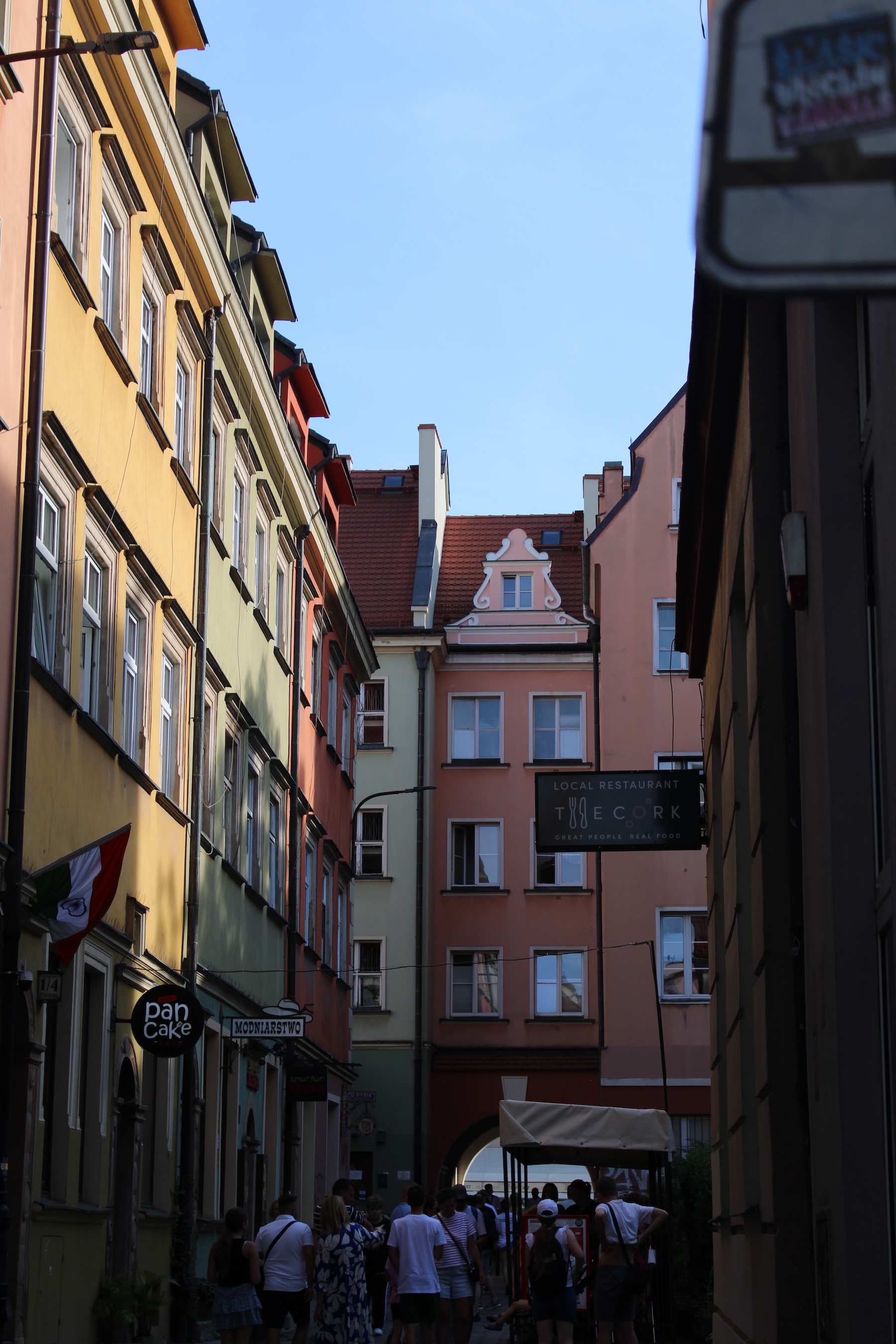 A busy alleyway is lit on one side by sunlight