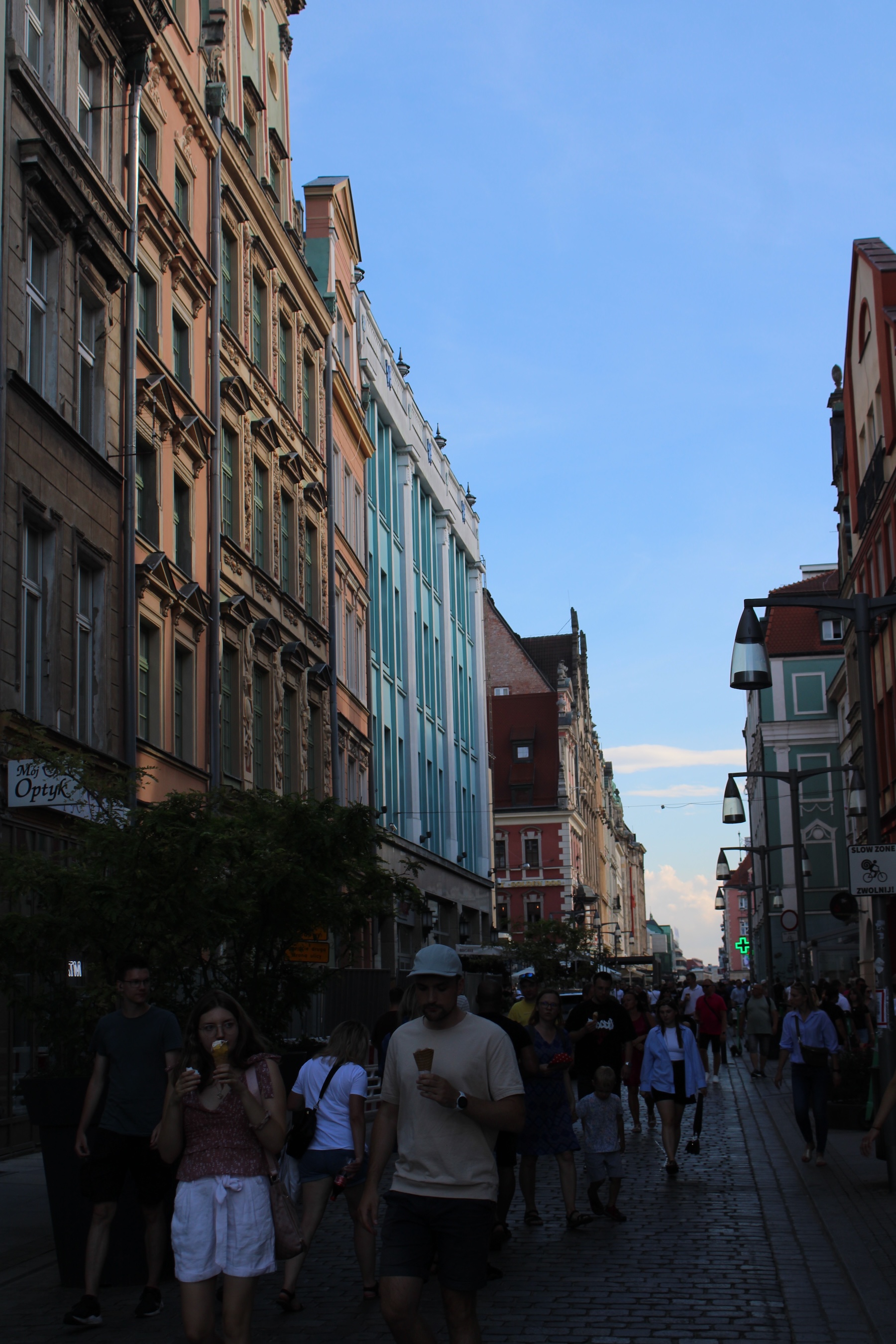 A busy tourist street is overlooked by multicolored buildings and a lightly clouded sky