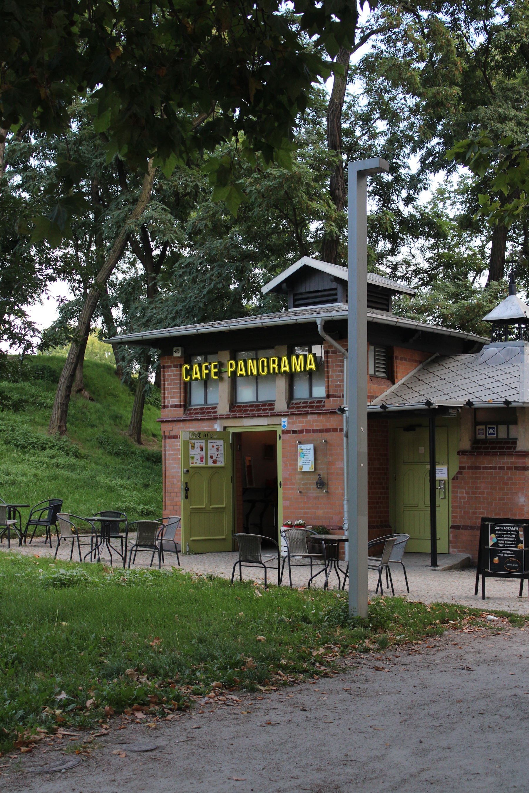 A neon sign that says Cafe Panorama adorns the side of a small park cafe
